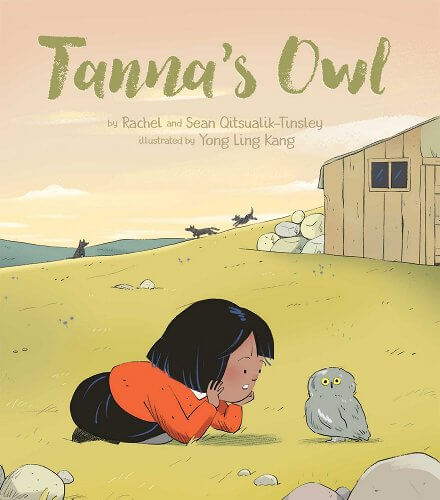 A small Indigenous girl with short black hair wears an organge sweater and kneels on the ground, staring at a gray owl who looks away from her.
